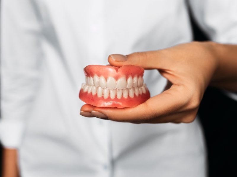 Dental prosthesis in the hands of the doctor close-up. Front view of complete denture Dental prosthesis in the hands of the doctor close-up. Front view of complete denture